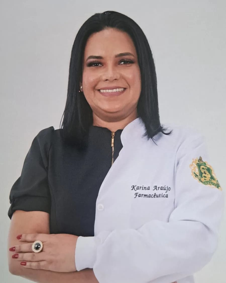 Karina Araújo, farmacêutica, sorrindo, de jaleco branco com o nome bordado